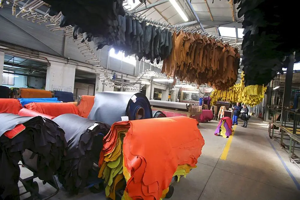 Tannerie avec des peaux colorées suspendues et empilées, travailleurs en arrière-plan.