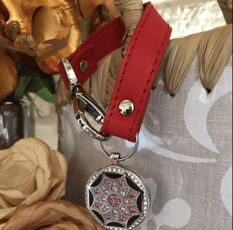 Porte-clés en cuir rouge avec pendentif orné de cristaux roses, accroché à un panier en osier.