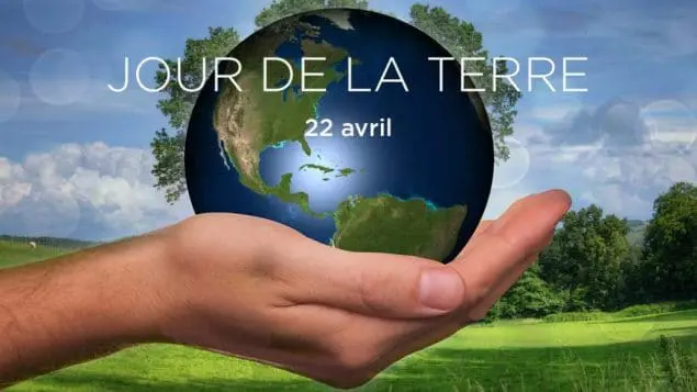Main tenant la Terre avec texte "Jour de la Terre, 22 avril" sur fond de paysage verdoyant.