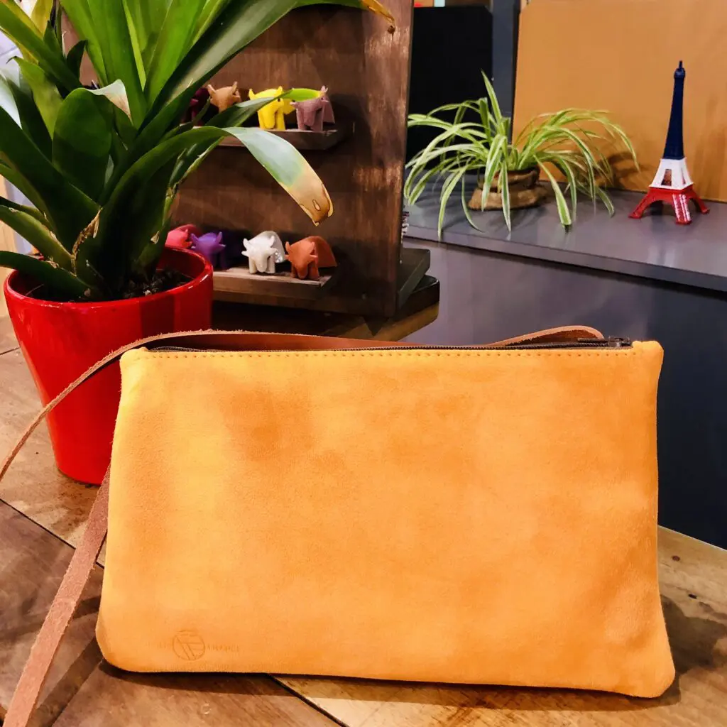 Sac en cuir orange sur une table en bois, à côté d'une plante en pot rouge et de petites figurines colorées.