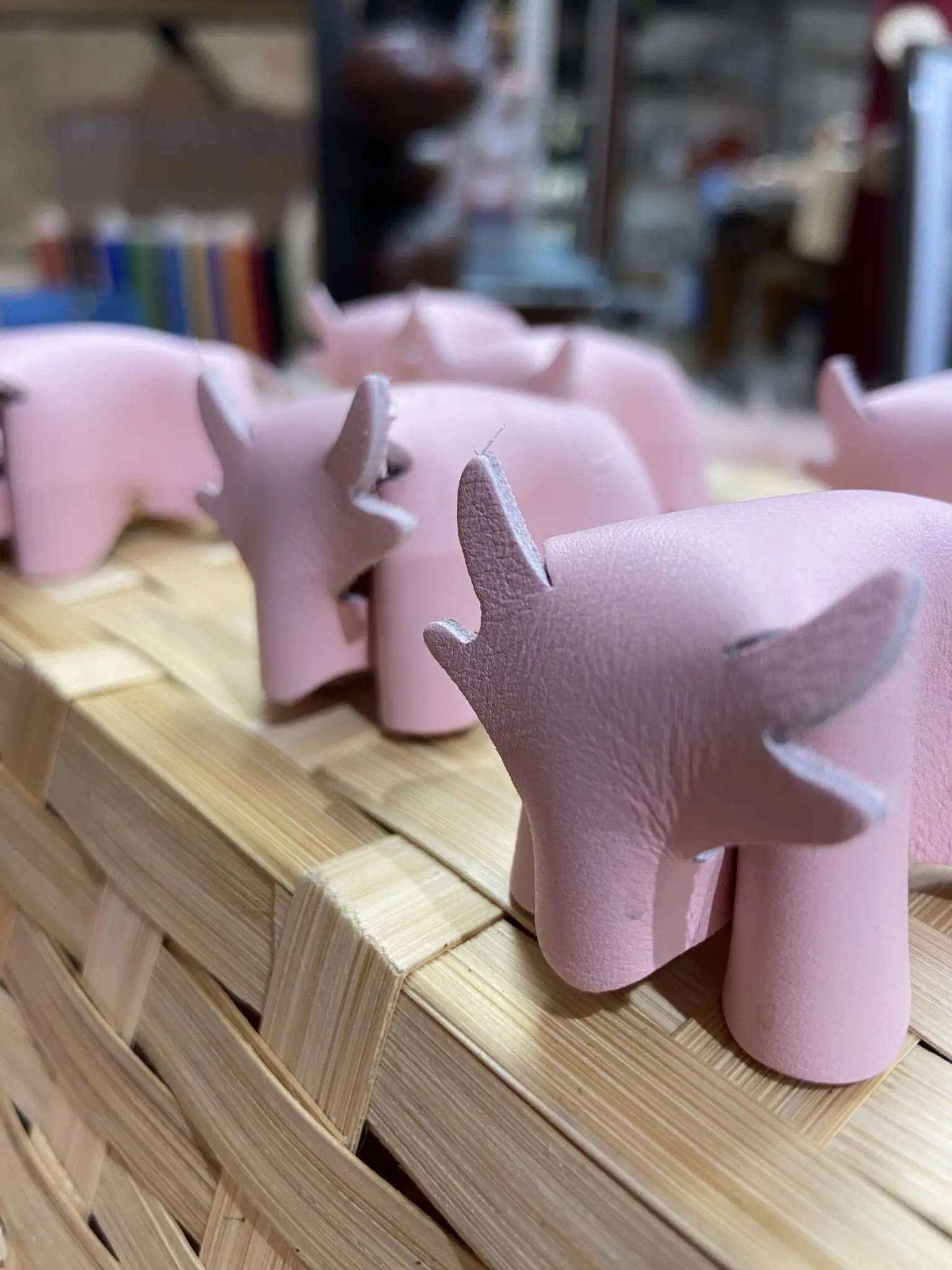 Petites figurines de vaches roses en cuir sur un panier en osier, avec des crayons colorés en arrière-plan.